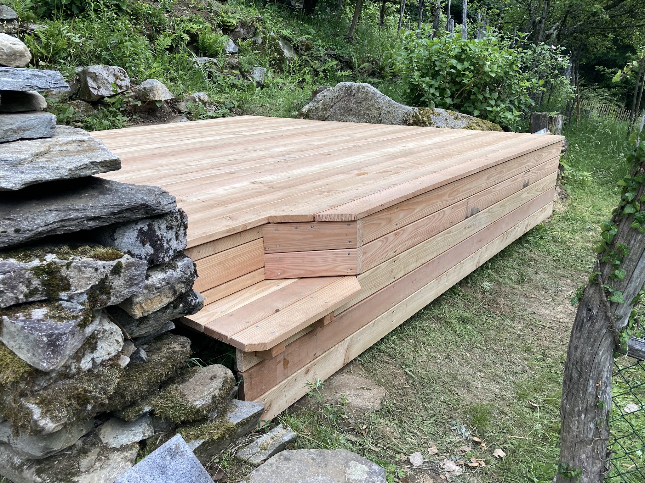 Holzterrasse mit Stufe an einer Natursteinmauer