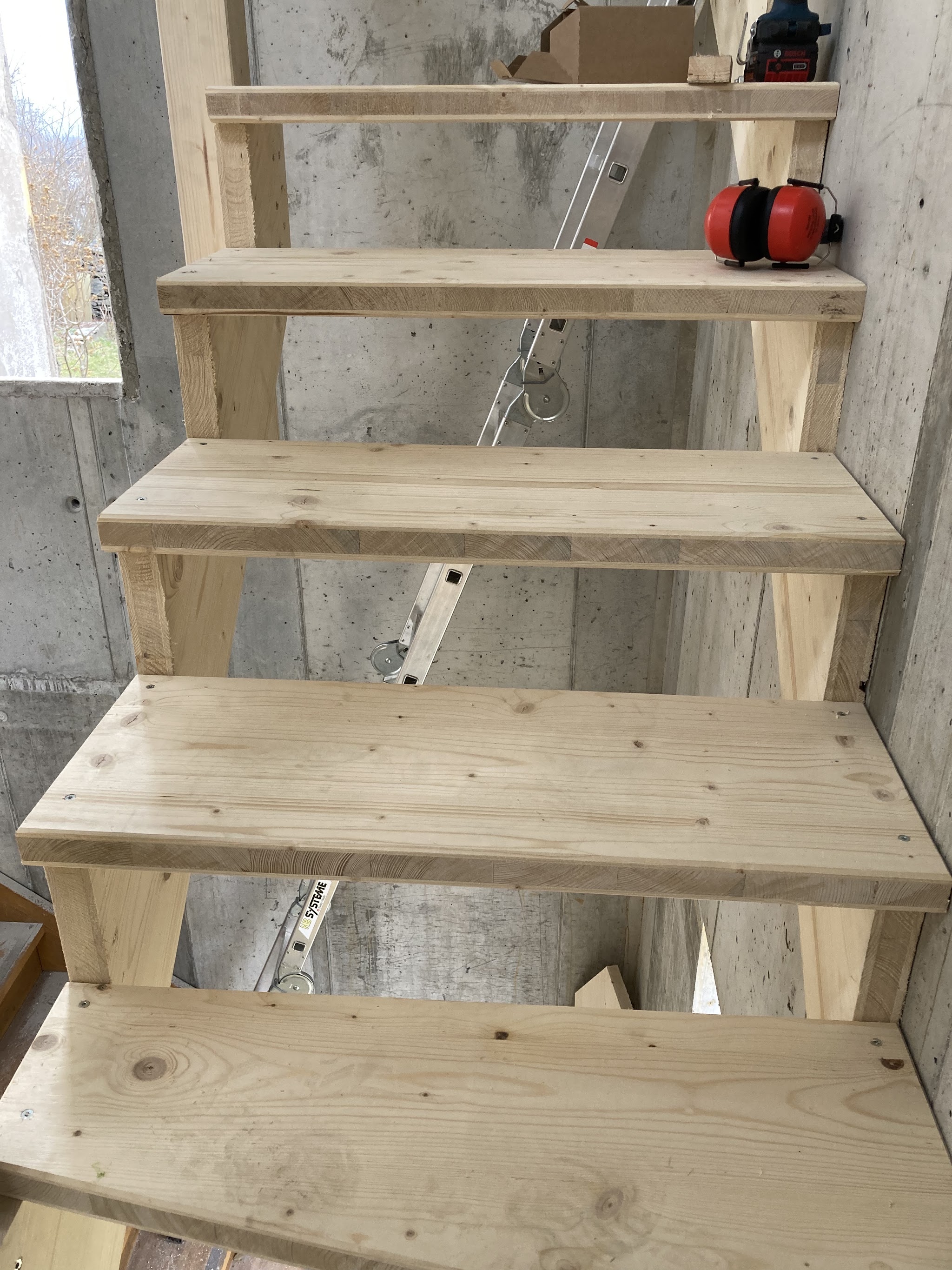 Holztreppe mit hellen Holztritten neben einer Betonwand