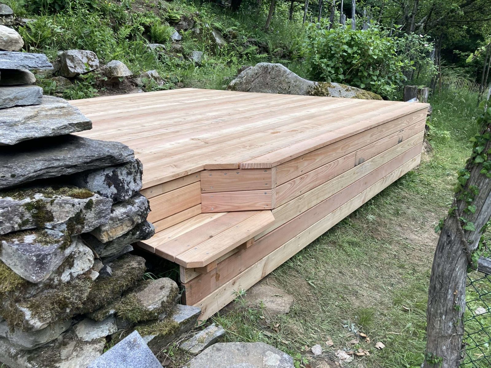 Sitzplatz aus Lärchenholz an einer Natursteinmauer
